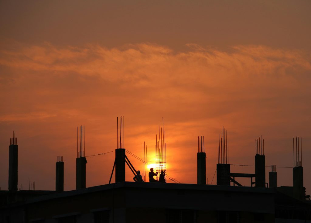 Silhouette of workers on a construction site against a vibrant sunset sky.